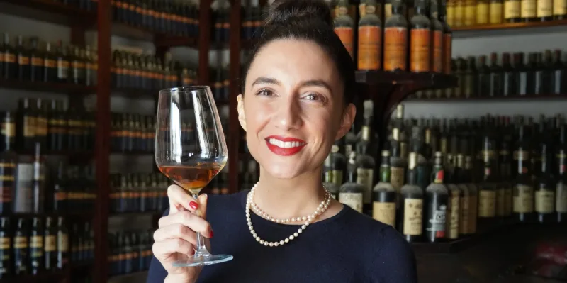 Giulia sorrindo e erguendo uma taça de vinho numa adega italiana.